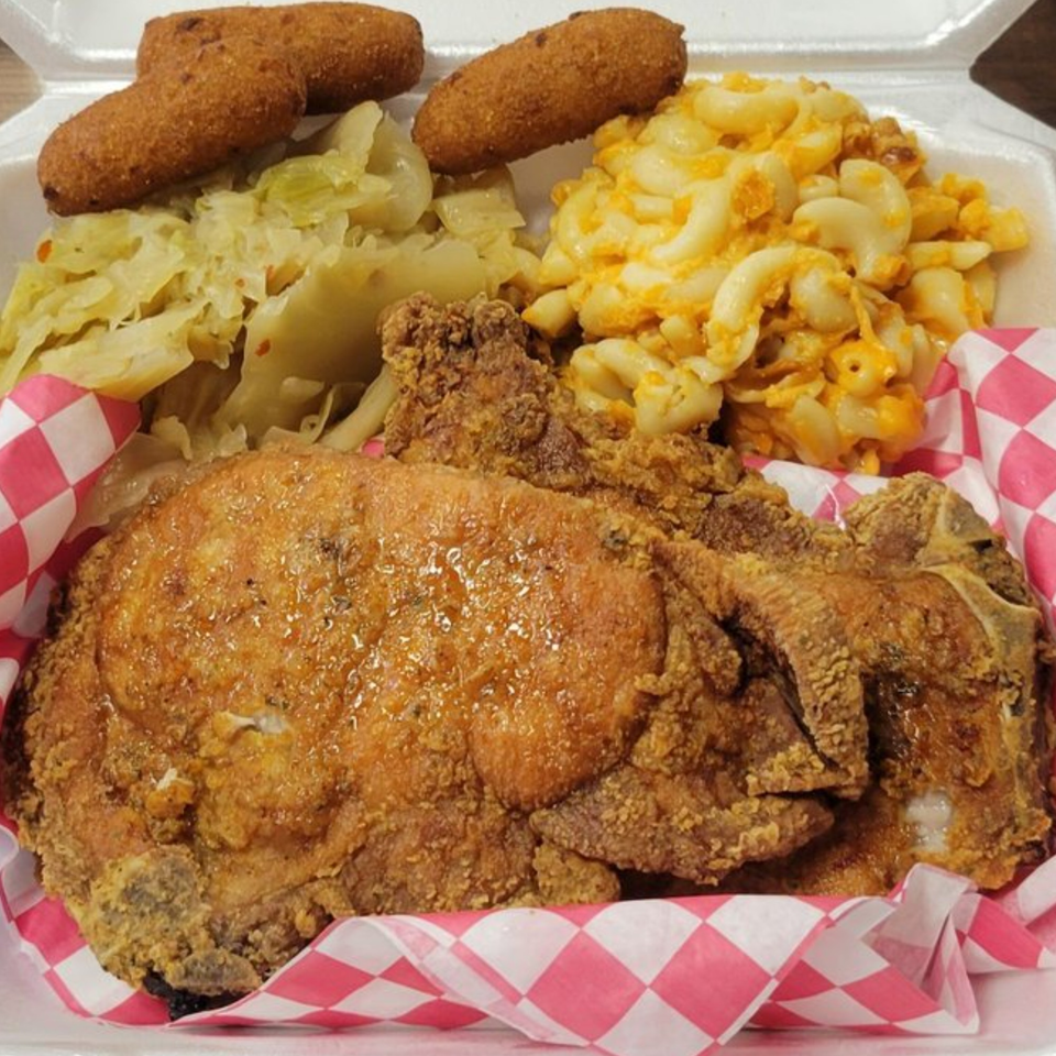 A soul food meal with fried pork chop, macaroni and cheese, cabbage, and hush puppies.