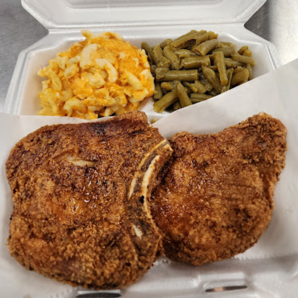 Two crispy fried pork chops with macaroni and cheese and green beans in a takeout container.