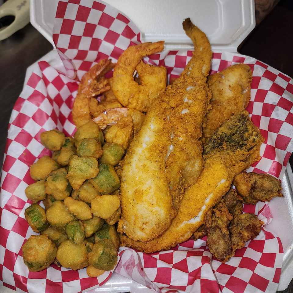 A takeout container filled with fried fish, shrimp, oysters, and okra on red and white checkered paper.