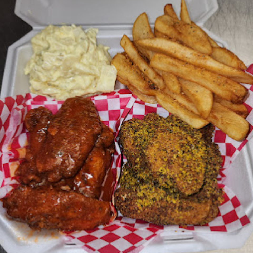 A takeout container with saucy and seasoned chicken wings, potato salad, and seasoned fries.