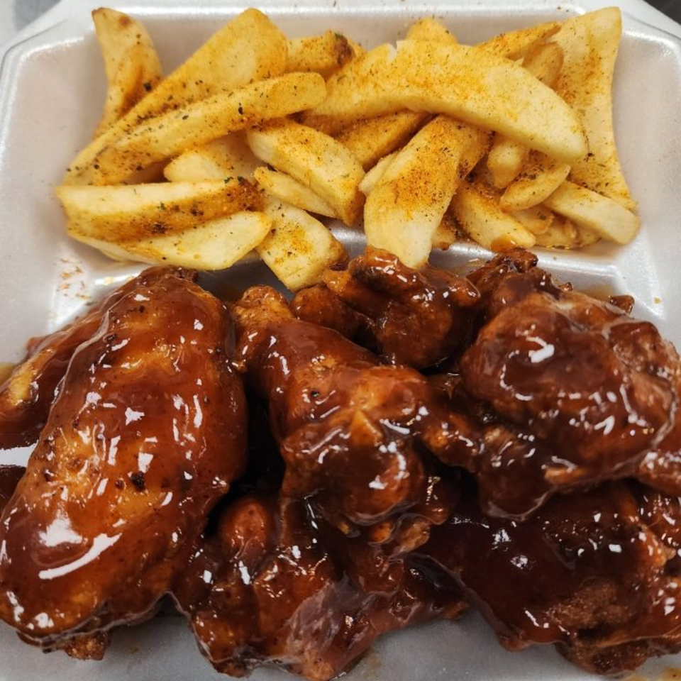 Levy's Soul Cafe's BBQ chicken wings with a side of seasoned potato wedges in a takeout container.